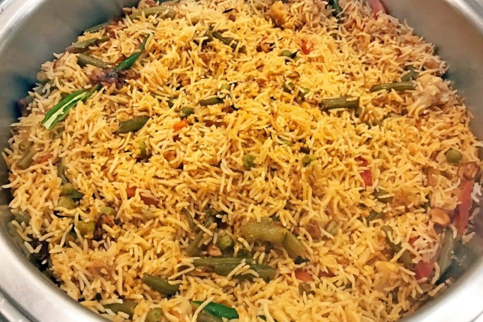 A silver bowl or pot filled with savoury rice and a few small pieces of vegetables.