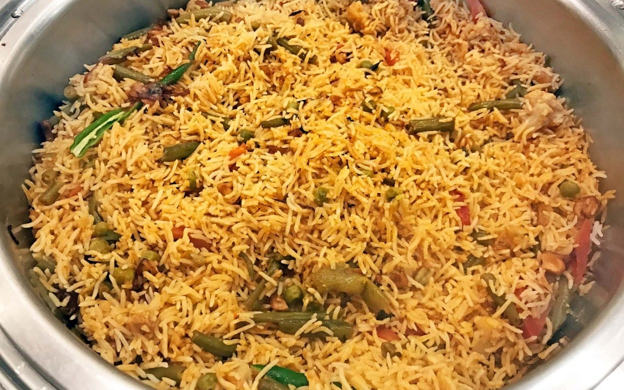 A silver bowl or pot filled with savoury rice and a few small pieces of vegetables.
