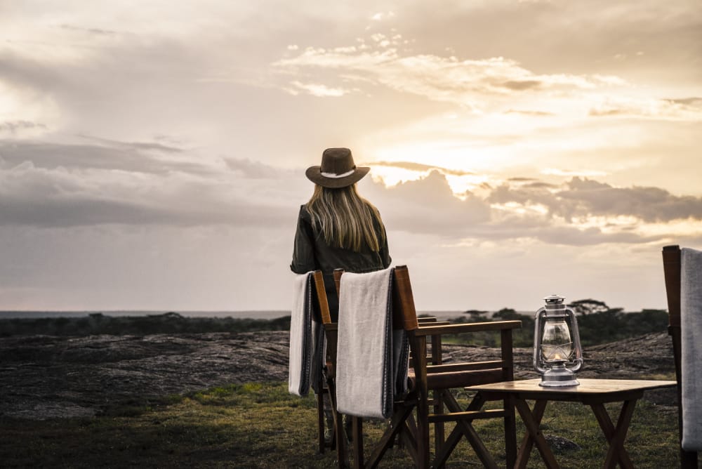 Woman watching the sunset in the Serengeti. There are few must-haves to pack with you on your Tanzania safari packing list.