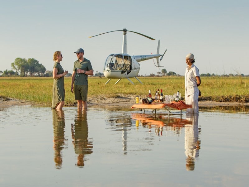A couple standing in a shallow waterway with a helicopter in the background.