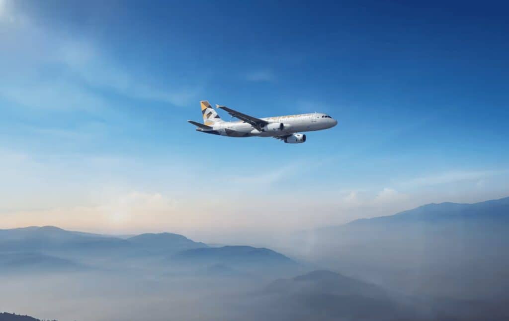Etihad Airways plane flying across blue sky over mountains