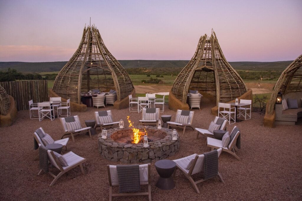 A firepit with chairs around it and wicker structures in the background with tables inside for dinner.