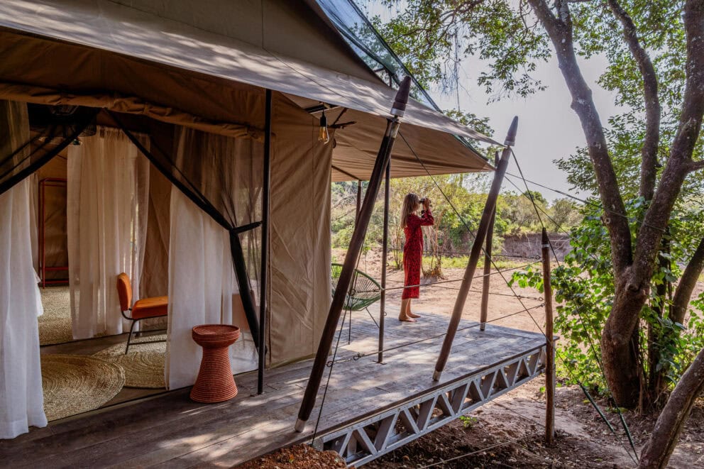 Woman standing on verandah looking through binoculars outside her safari tent