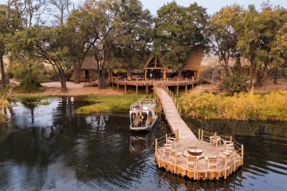 A safari lodge with a jetty going out into the water and a boat on the left-hand side in the water.