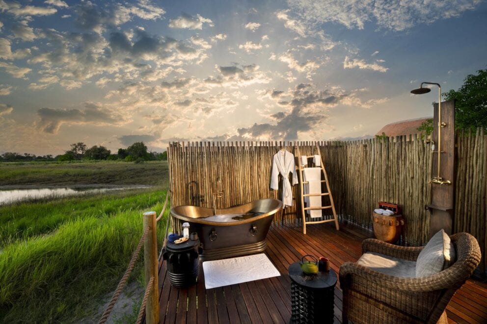 An outdoor bathroom in the Okavango Delta with a bathtub, shower, chair, and bathrobe hanging from the fence.
